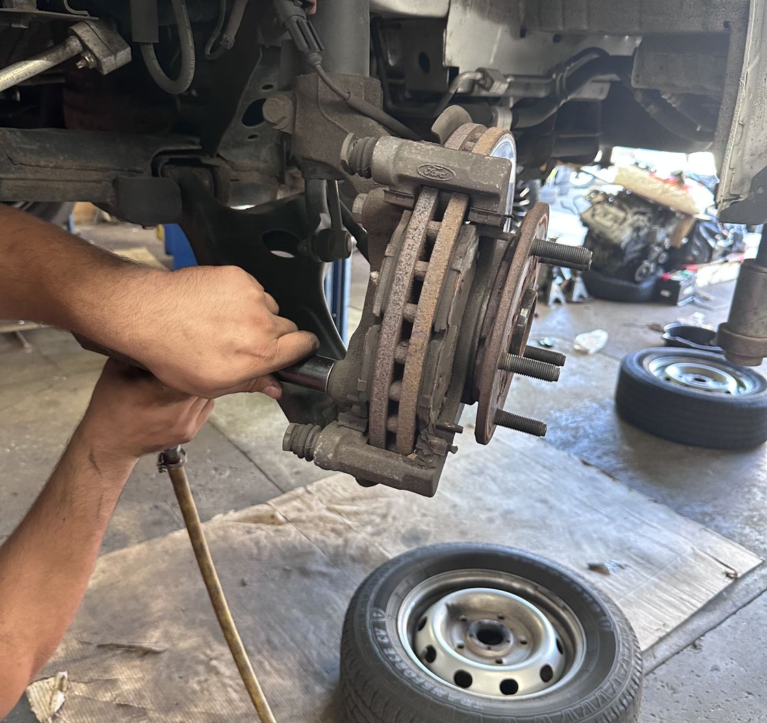 Hands lifting the caliper and worn rotor off the hub with the wheel down on the shop floor