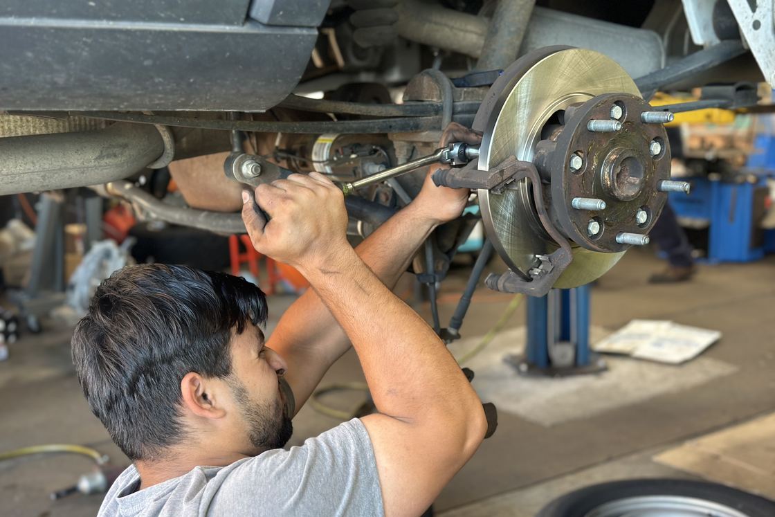 A Yardville Auto Repair technician working on a brake rotor with the wheel off and the vehicle raised in the bay